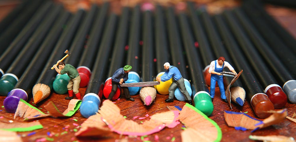 Little people, men, sharpening color pencils.