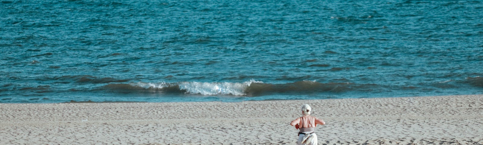 Older woman walks down the beach toward the ocean
