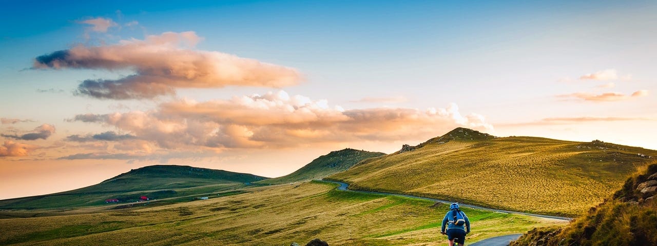 Man on a mountain road cycling towards the rising sun.