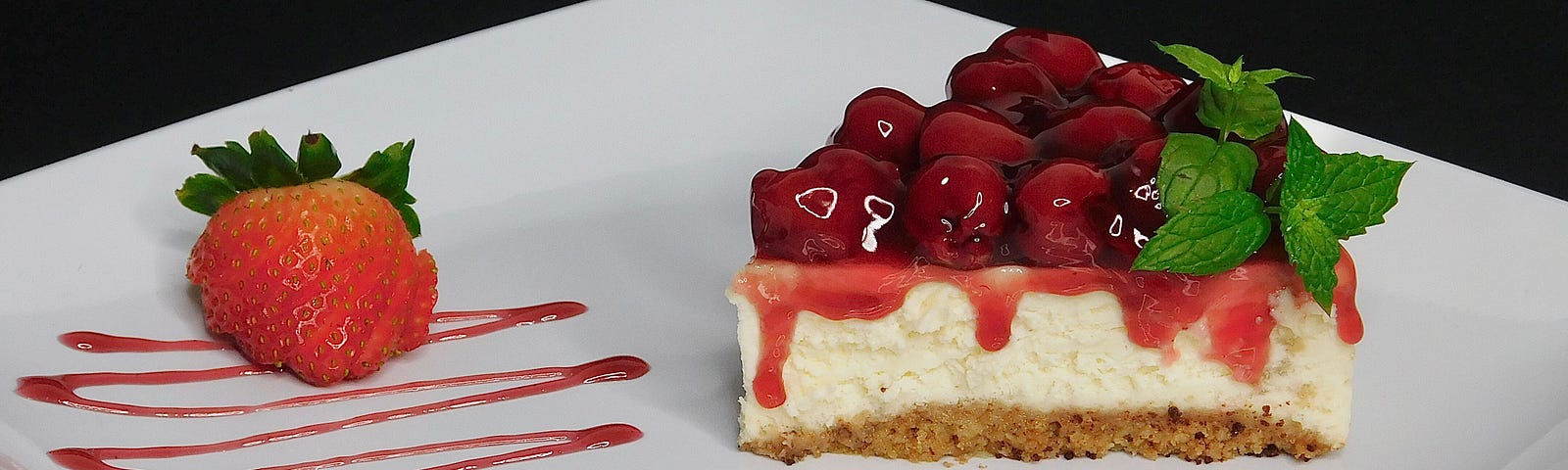 plate with cherry-topped cheesecake, the plate decorated with red syrup and a strawberry