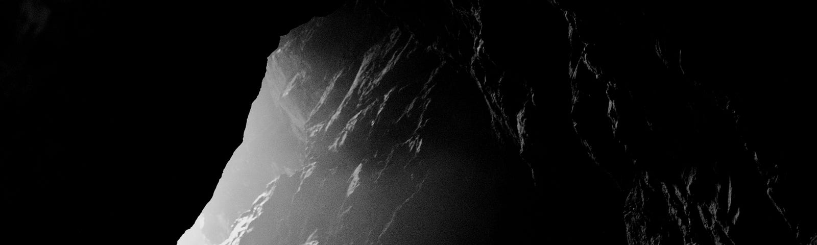 a cave entrance from the inside. bright light illuminates craggly rocks.