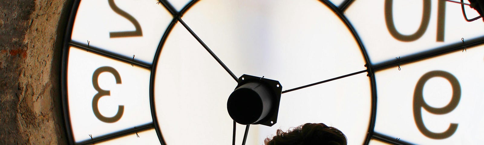 A dark silhouette of man in front of a giant window clock.