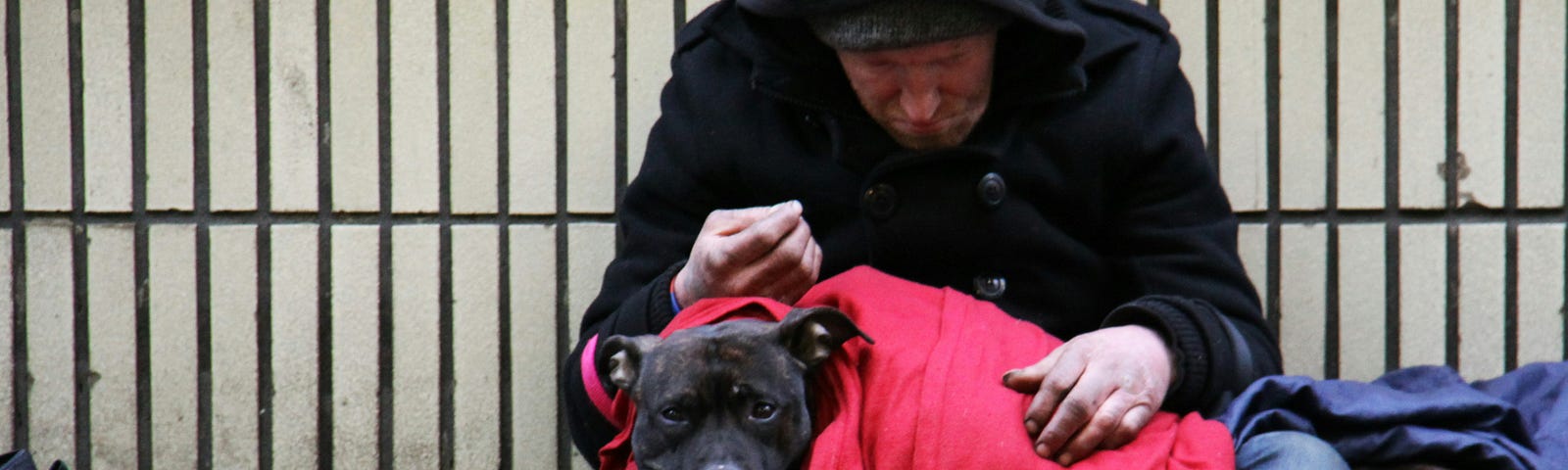 A homeless man on a sidewalk with a dog in his lap