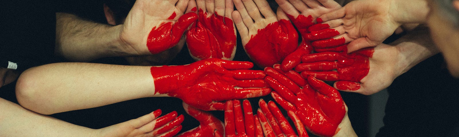15 hands placed together with red paint on them resembling the shape of love.