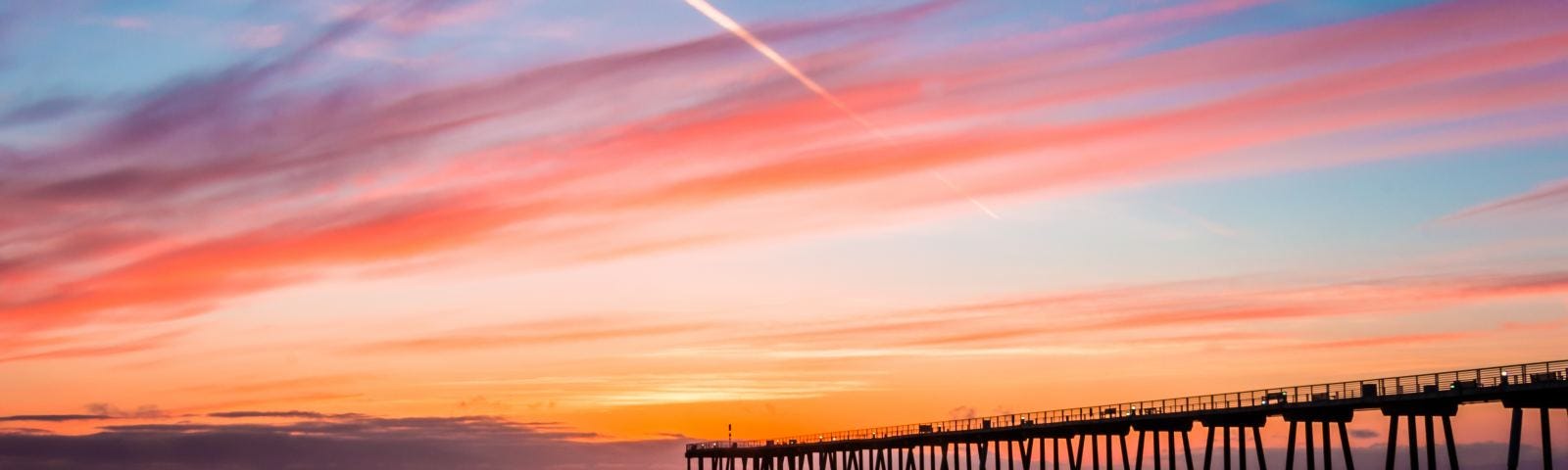 A view of Hermosa Beach during a sunset with a bridge blocking the view.