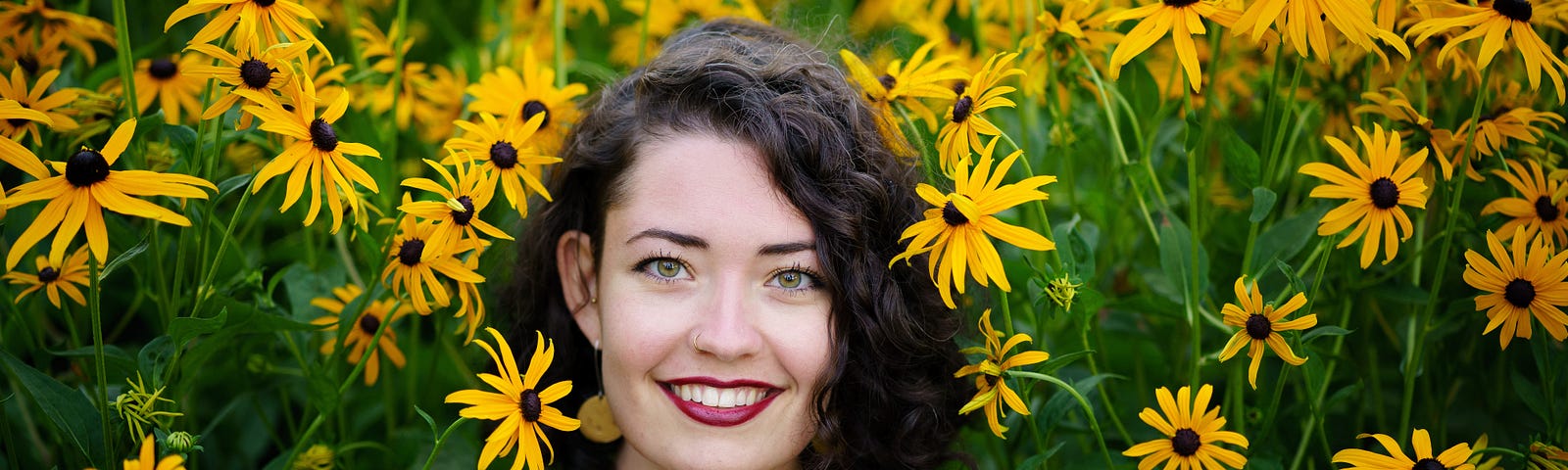 A woman smiles among a garden of daiseys.
