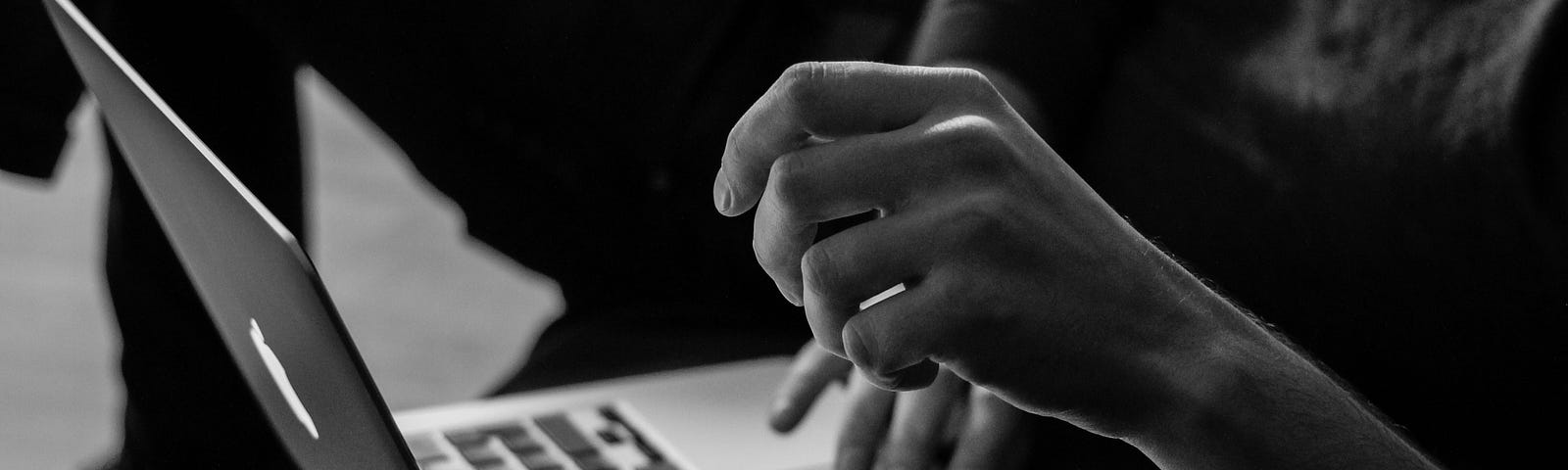 Black and white image of hands and a laptop.