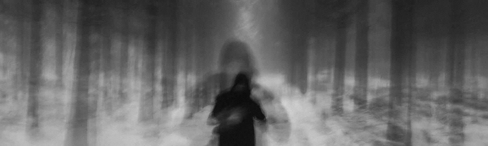 A blurry black and white image of a person in the woods.