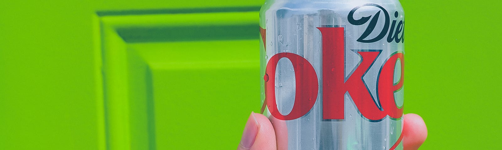 A hand holding a can of Diet Coke in front of a bright green door