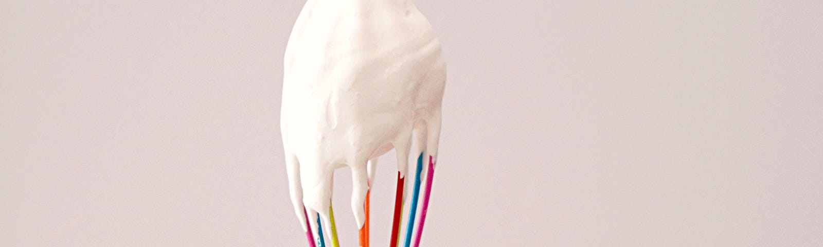 A hand holding rainbow whisk with white batter on the top