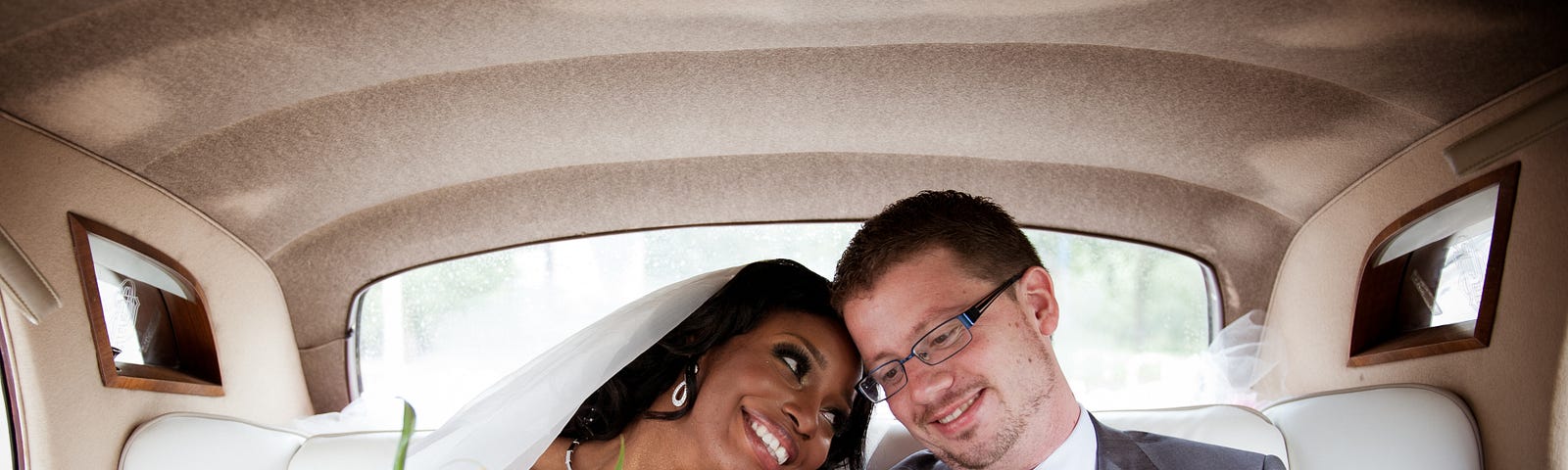 image shows a newly wedded interracial couple in the back of a limo. The female is black and her head is resting on the shoulder of her new husband. The man is leaning towards her with a happy smile on his face.