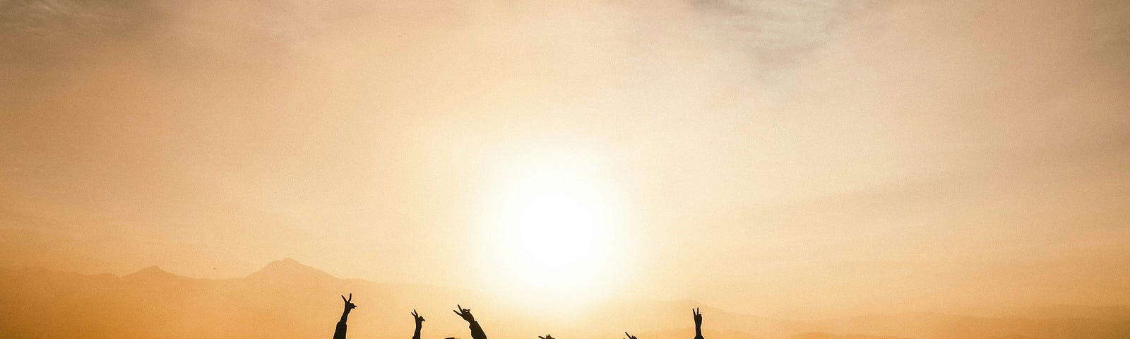Six people stand on a hill silhouetted by the light of the rising sun.