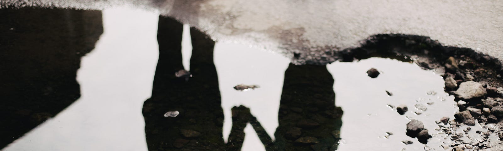 A couple reflected upside down in a puddle of water, holding hands.