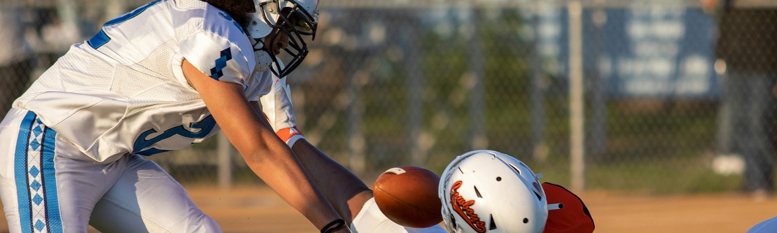 An ofensive football player with the ball his pulled down and tackled by two opponents