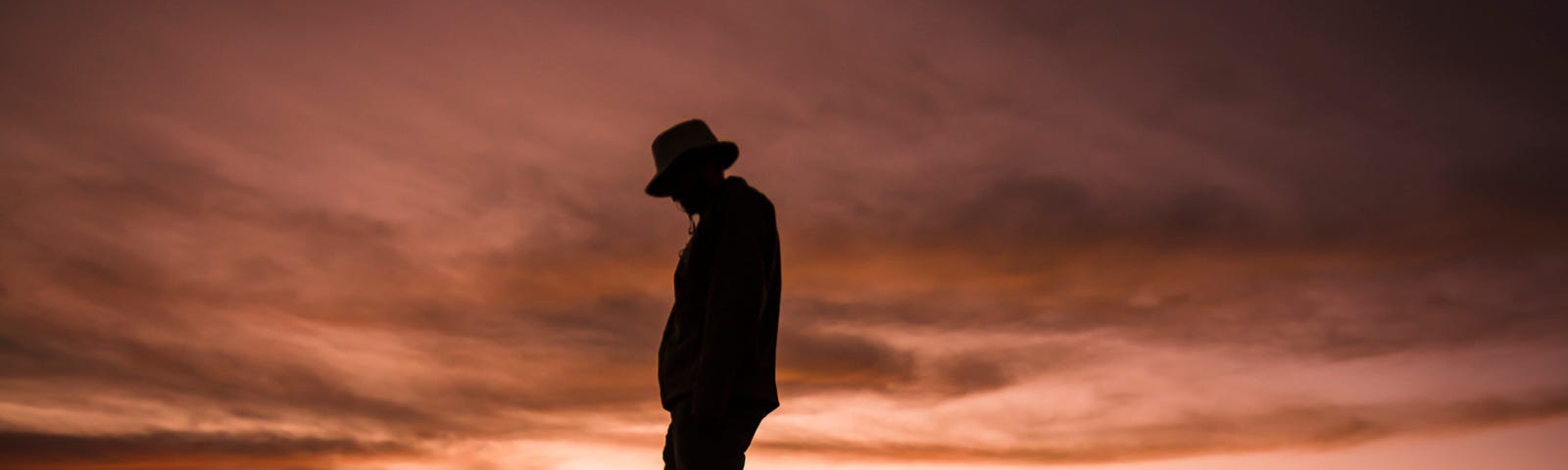 A dark silhoutte of a man walking in front of a vibrant sunset.