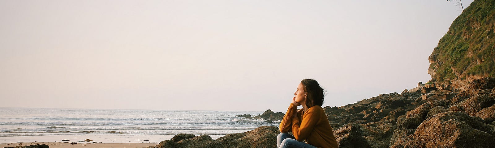 Woman sitting on beach looking off into the distance.