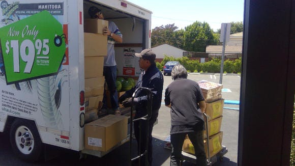 Men unloading produce boxes from a U-Haul trailer