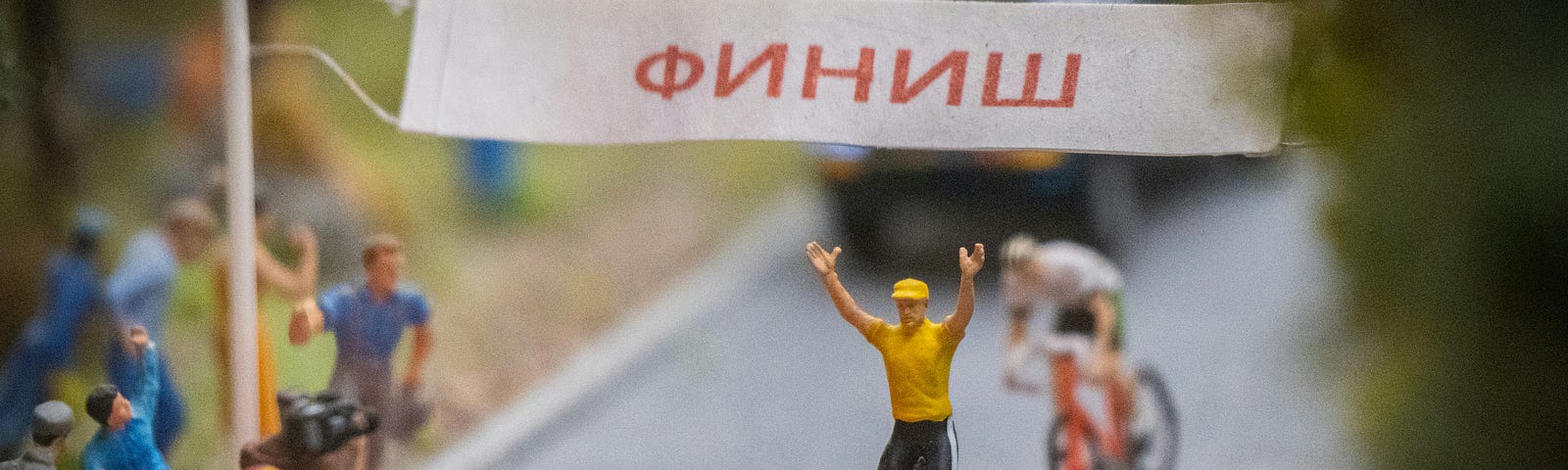 Cyclist crossing the finish line, with both hands raised in victory.