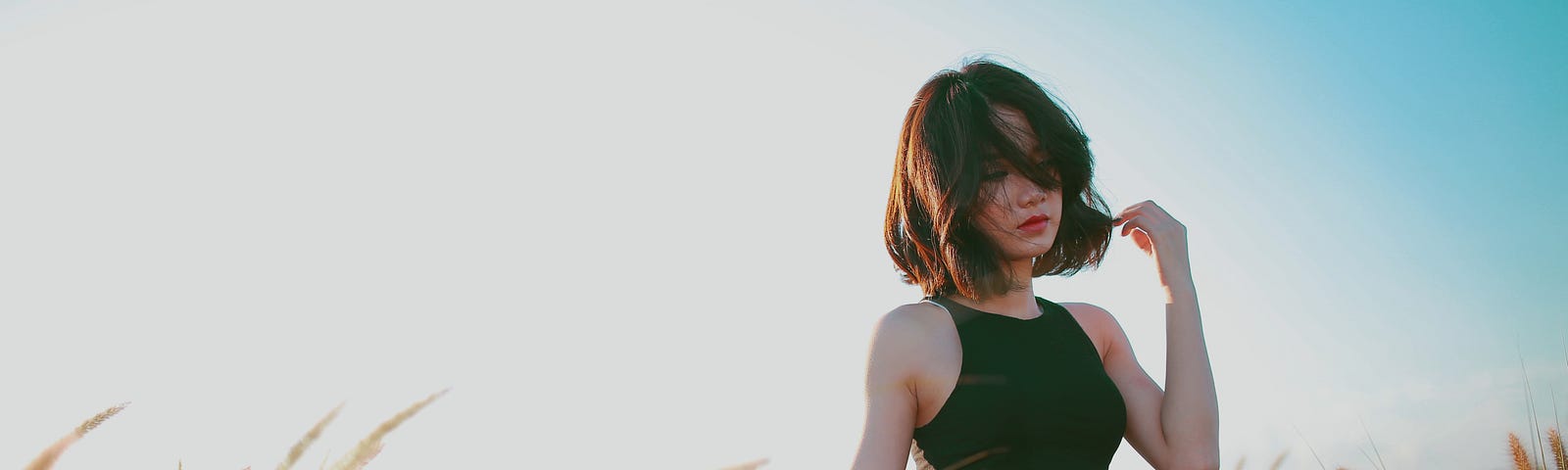 A woman holding her hair blowing in the wind as she walks through a field of plants