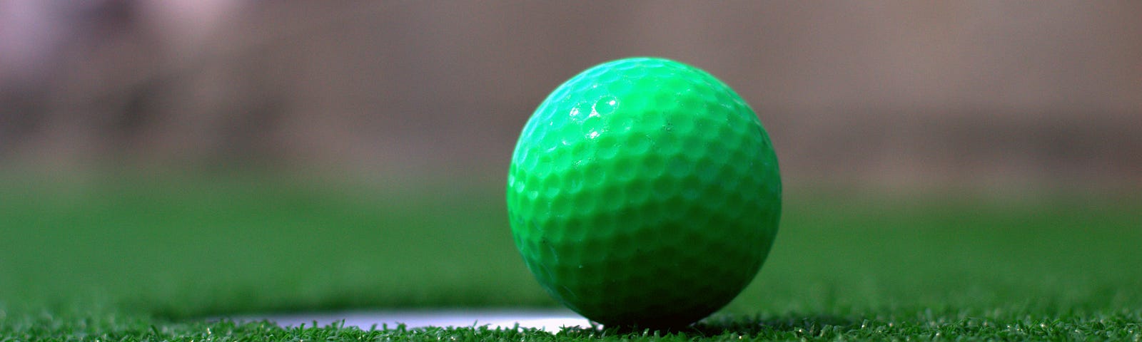 A green golf ball on the edge of a cup.