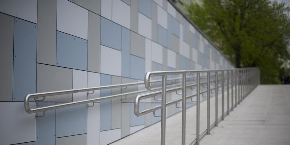 A concrete ramp with a metal railing next to a tiled wall