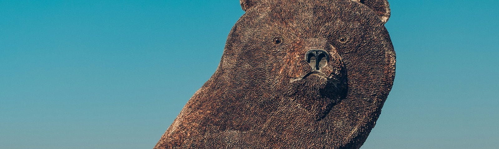 Rock sculpture of a bear against a blue sky.