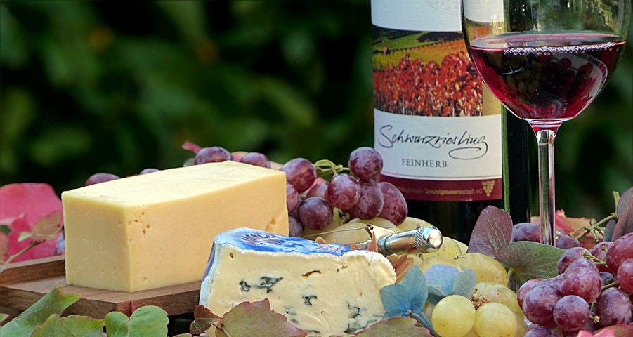 Table with cheeses, grapes fruits, and a bottle and half-a-glass of wine.