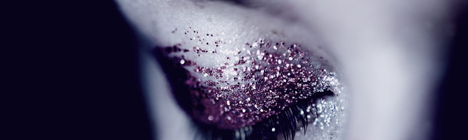 Purply dazzling eyeshadow glitter on a closed eyelid of an attractive woman only showing a partial quarter of her face.