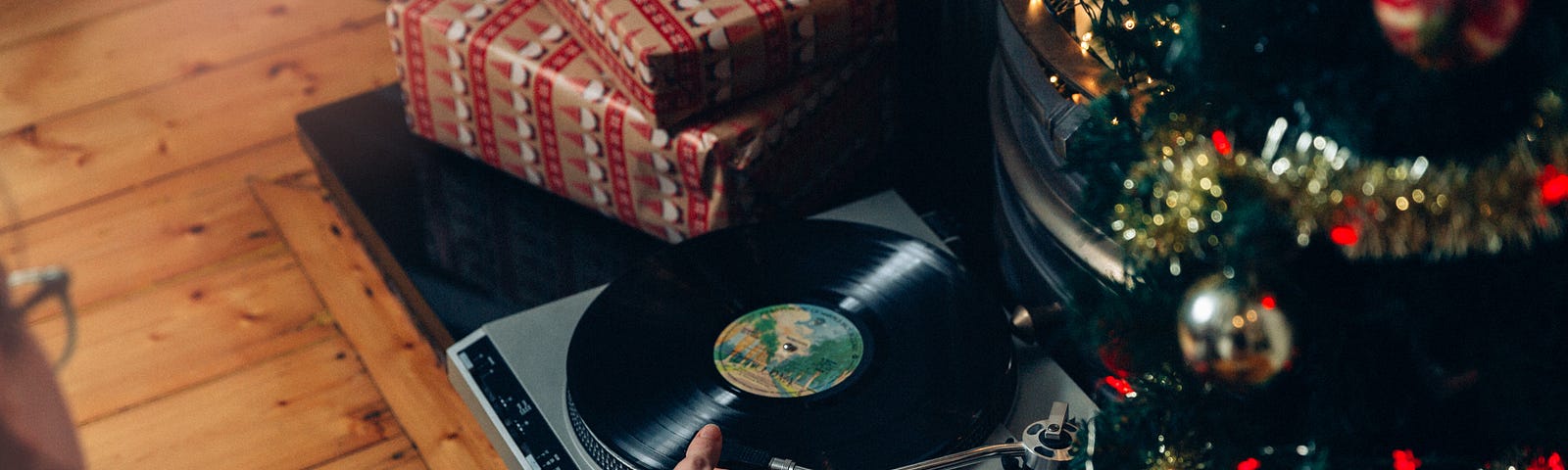 This shows a record player underneath a Christmas tree. A woman is putting a record on to play.