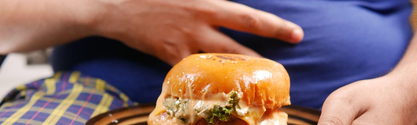 Man holding cheesy burger in front of large stomach