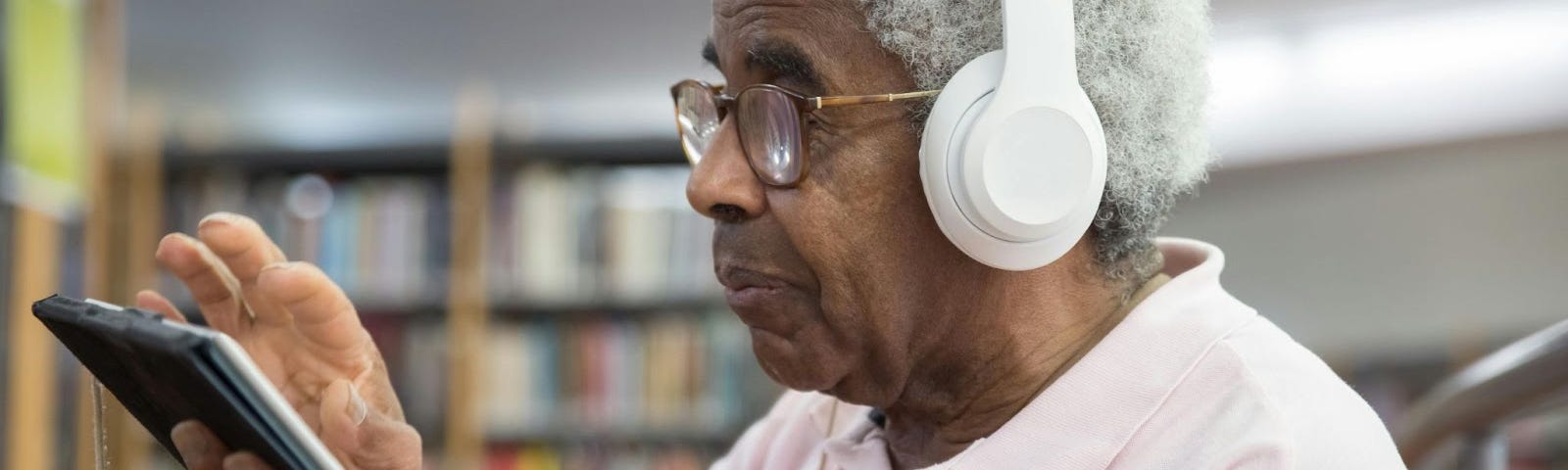 An elderly man with white hair and dark complexion wearing earphones navigate his fingers across an electronic tablet