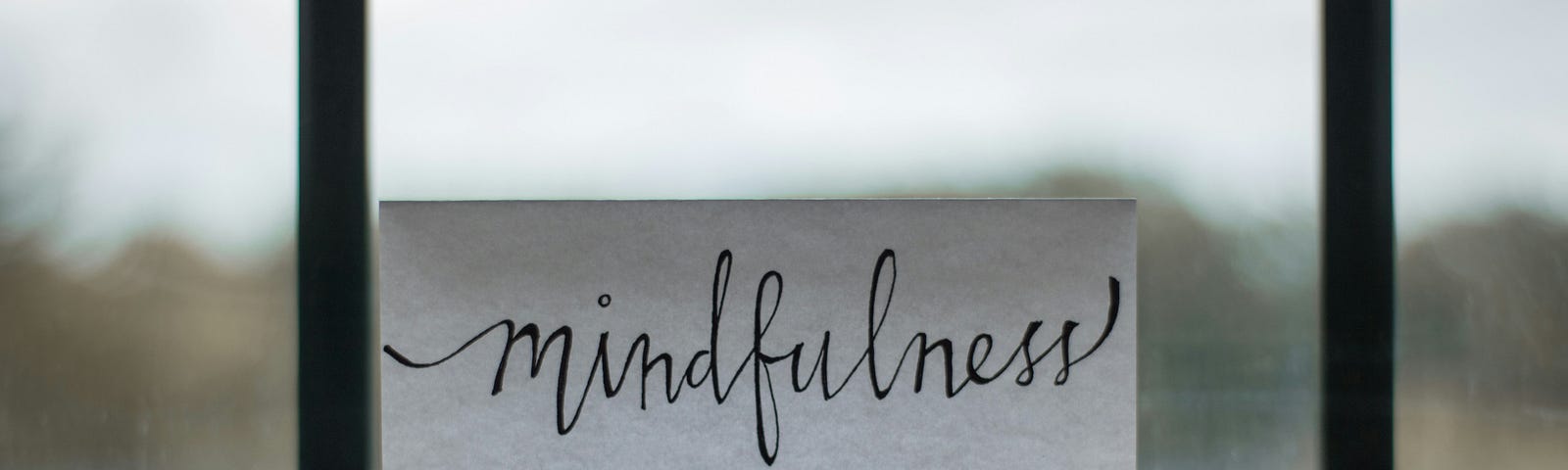 mindfulness written on a piece of white paper sitting on a desk. There is a window behind the paper.
