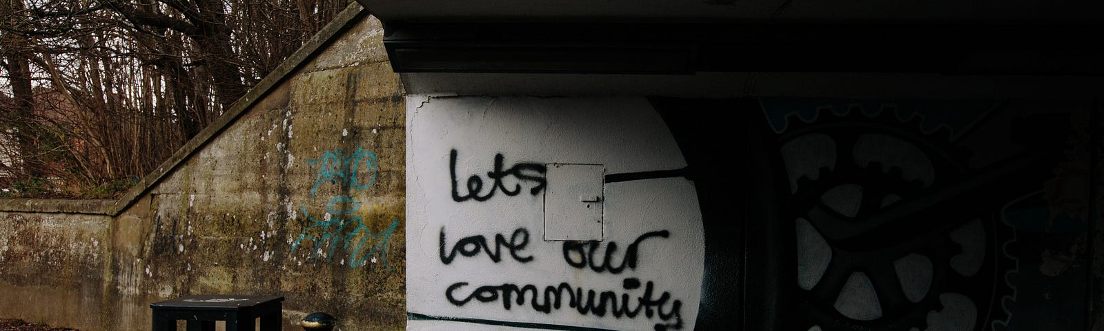A picture of a street under a bridge where the graffiti says, “Let’s love our community”