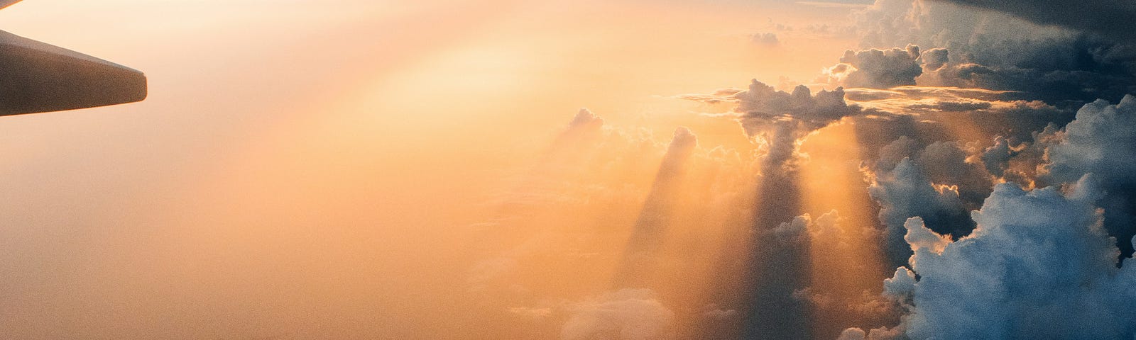 View of rear of plane while traveling mid flight above the clouds with sun shining in the distance