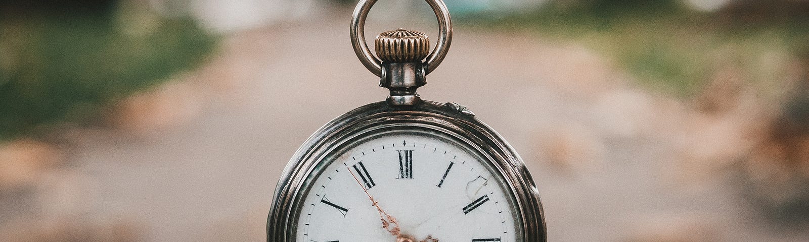 Old fashioned watch on chain, dangling free with a blurry outdoor scene in background