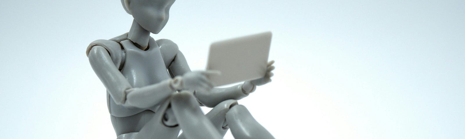 A robotic-looking plastic figure sitting on the floor holding a tablet.