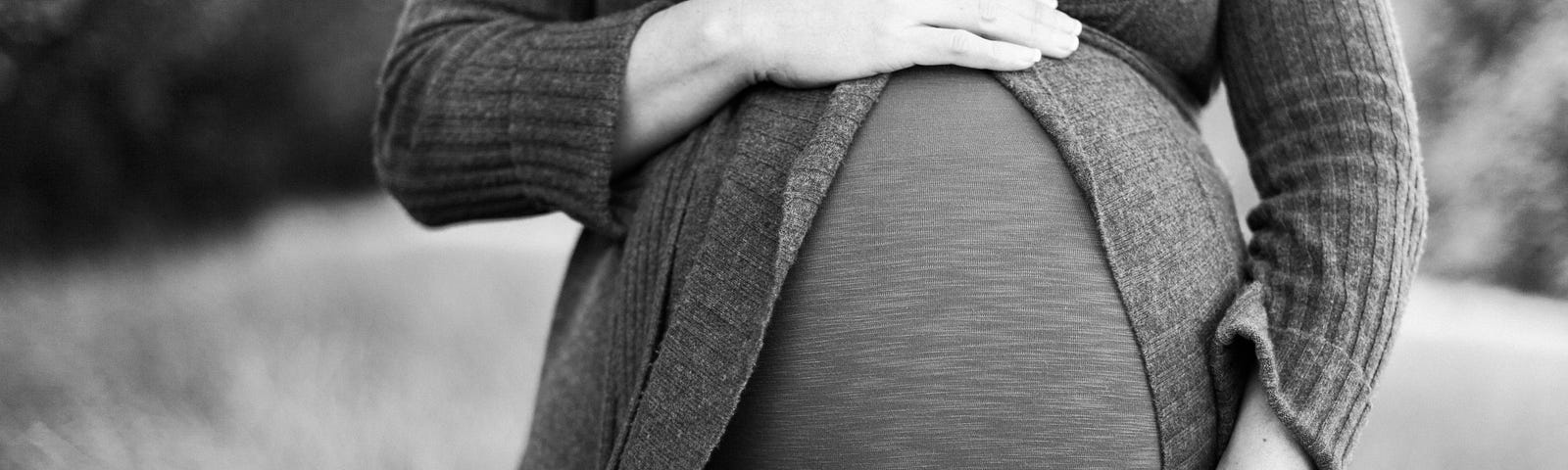 A pregnant wife with her hands on her belly. Photo in black and white.