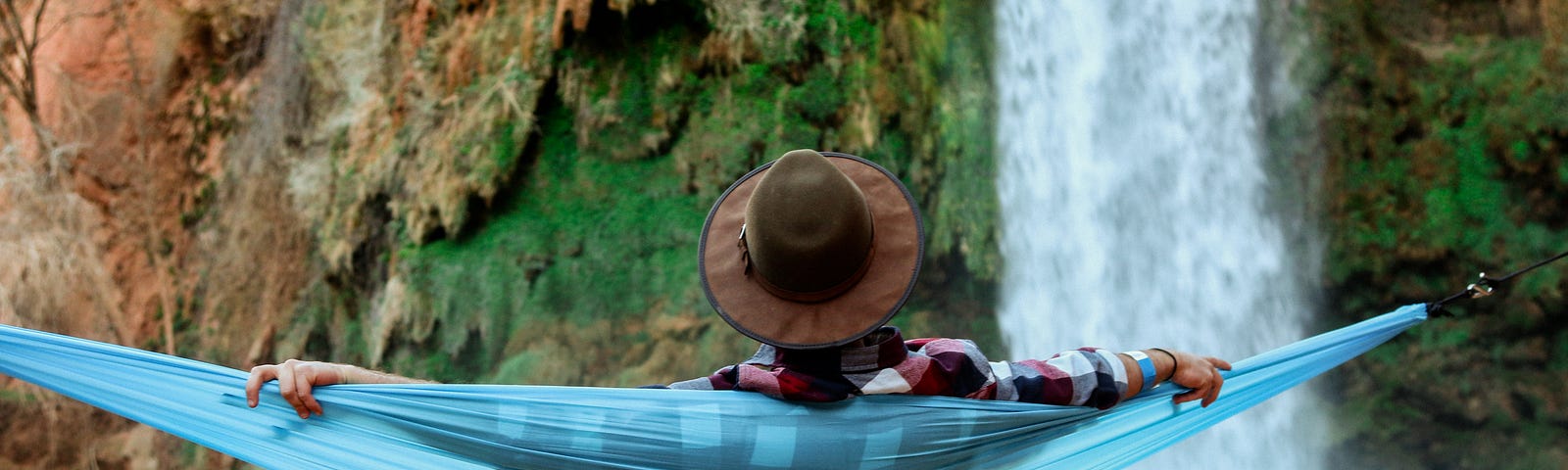 Young creator and entrepreneur wearing a hat and shorts relaxing on a net next to a waterfall and enjoying the revenue benefits of multiple passive income streams.