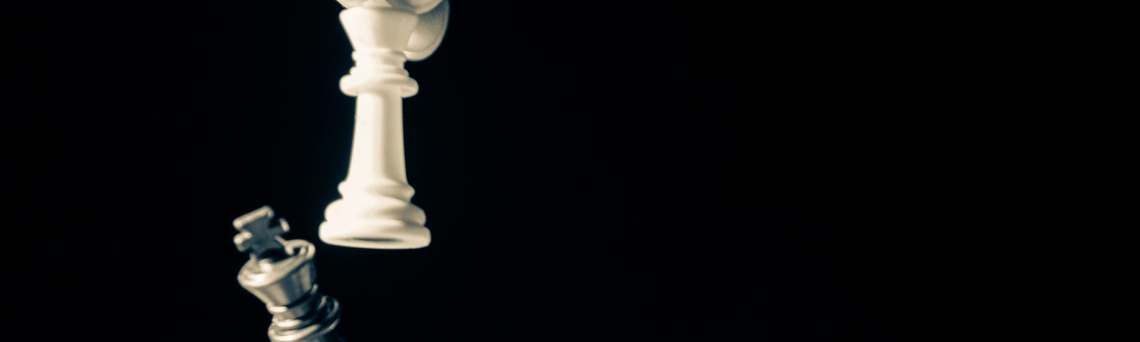 A picture of a person holding a white chess piece and tipping over another black chess piece.