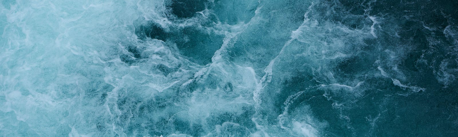 Turbulent sea from above — with some parts bluer, some whiter, it’s unclear what is going on but there are whirls and waves and foam