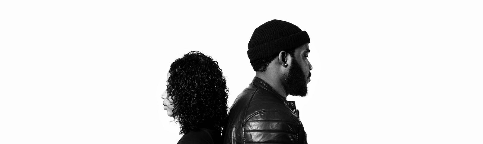 A black and white image of a Black couple standing back to back.