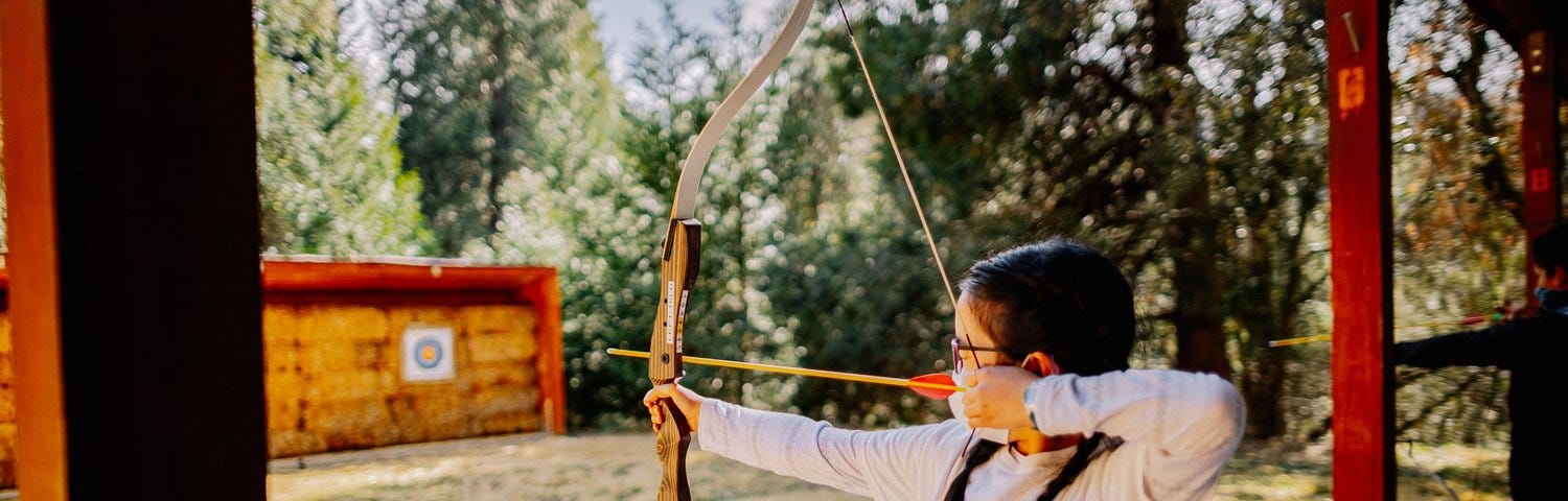 girl with bow and arrow aiming at target
