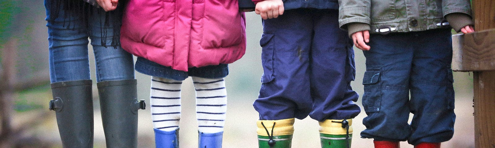 Children standing side by side wearing rain boots