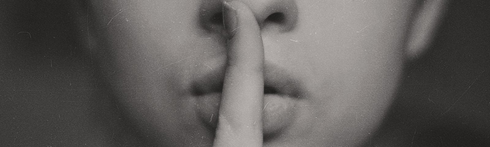 Image of a woman with a finger over her mouth making the “quiet” gesture.