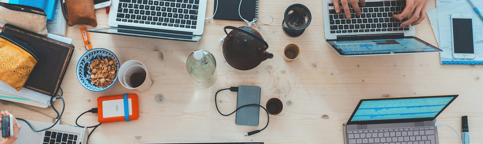 A tabletop scattered with laptops, phones, hard drives, portraying a busy work or study session