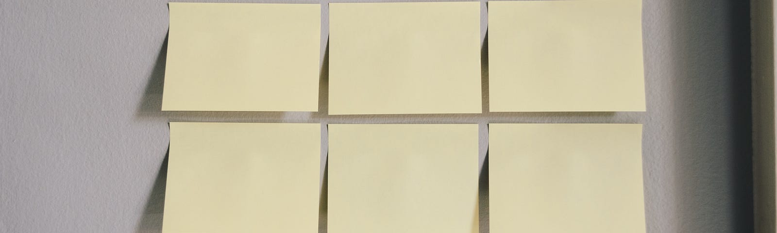 A series of blank post-it notes hanging on a wall with one being removed by a hand wearing dark nail polish.