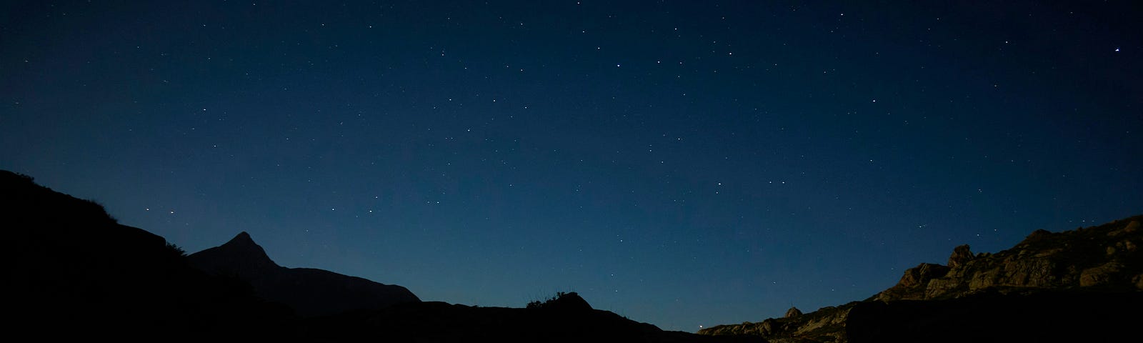 A serene night scene featuring a starry sky reflected in a calm body of water, surrounded by dark silhouettes of mountains.