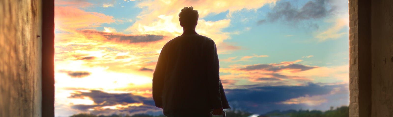 man stood with a suitcase looking out at a beautiful sunset