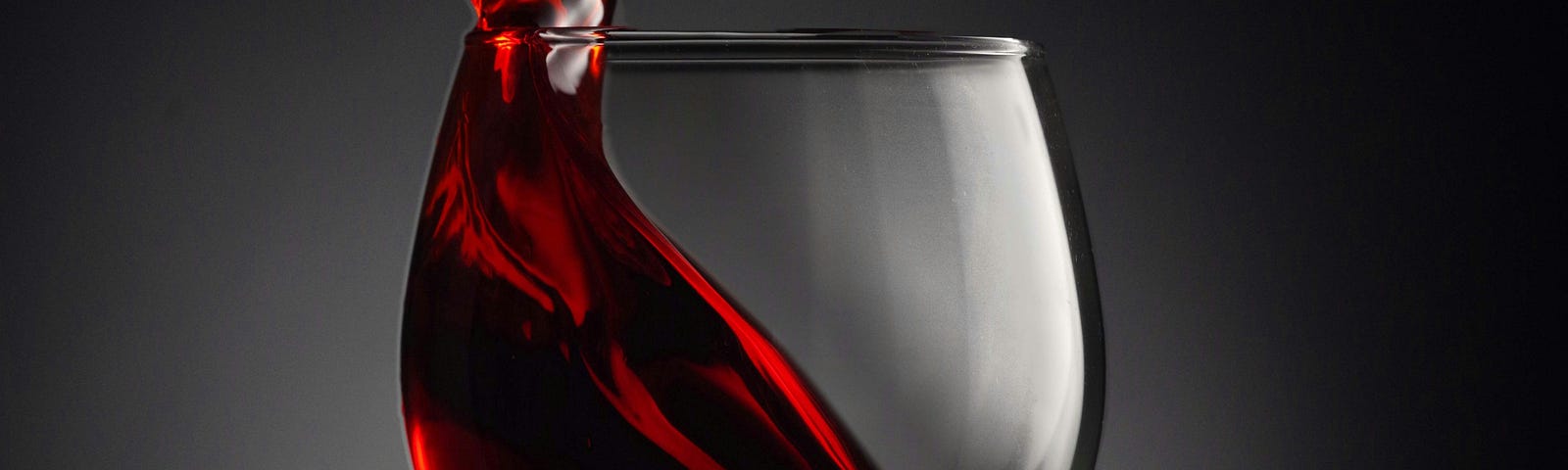 A glass of red wine. The fluid splashes up and out of the left side of the glass and drips down the right side. In this essay, I will delve into the various factors that could be behind the infamous headache after drinking red wine, exploring the intricate interplay of histamines, sulfites, tannins, and more. We’ll then look at the new study.