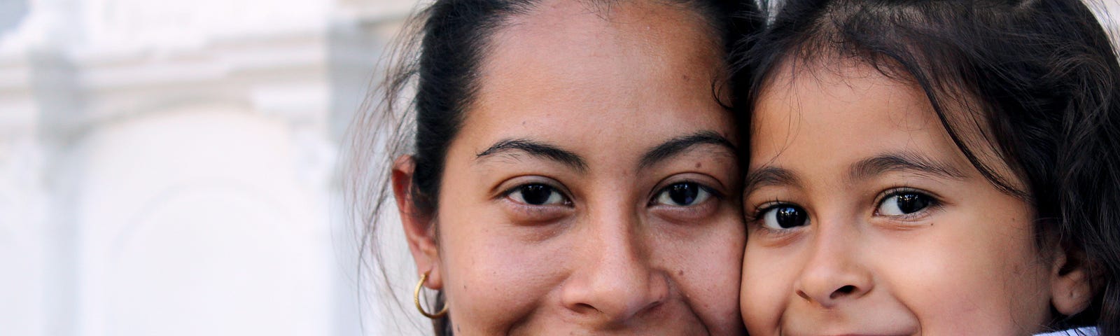 A woman smiling, holding a little girl who is smiling.